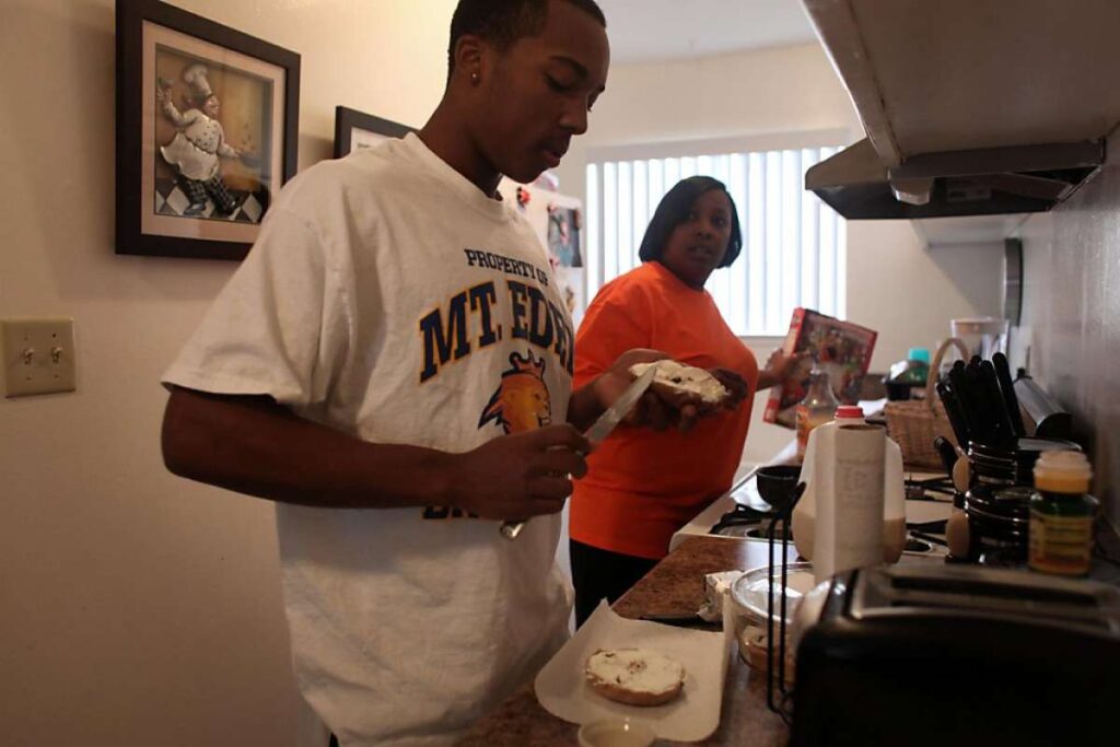 Mother and son prepare meal in modest kitchen.