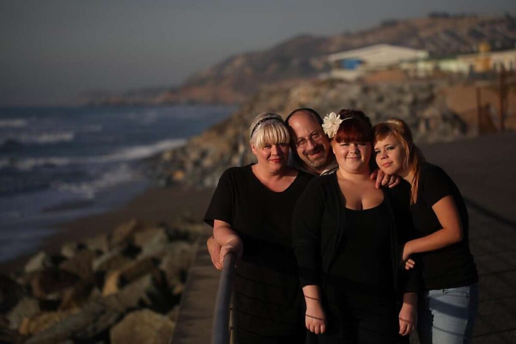 Family of four poses for photo near beach.