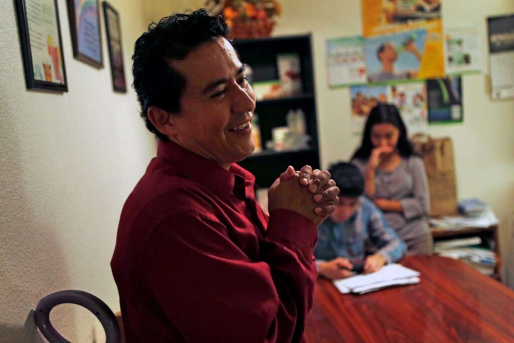 Man smiles at table with children in background.