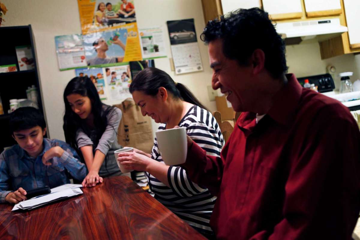 Family laughs together at kitchen table while enjoying beverages.
