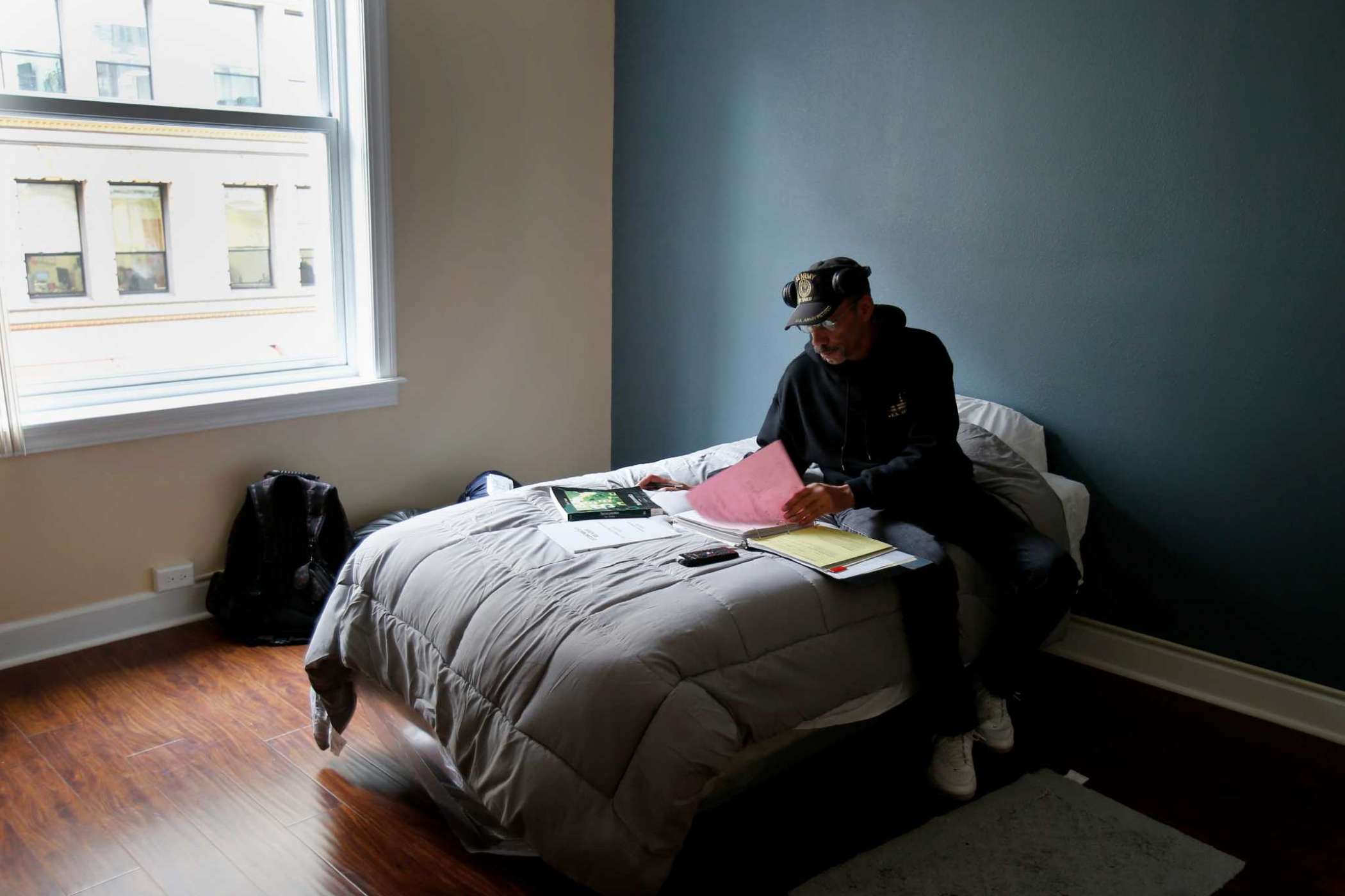Man sitting on bed looking over paperwork in binder.