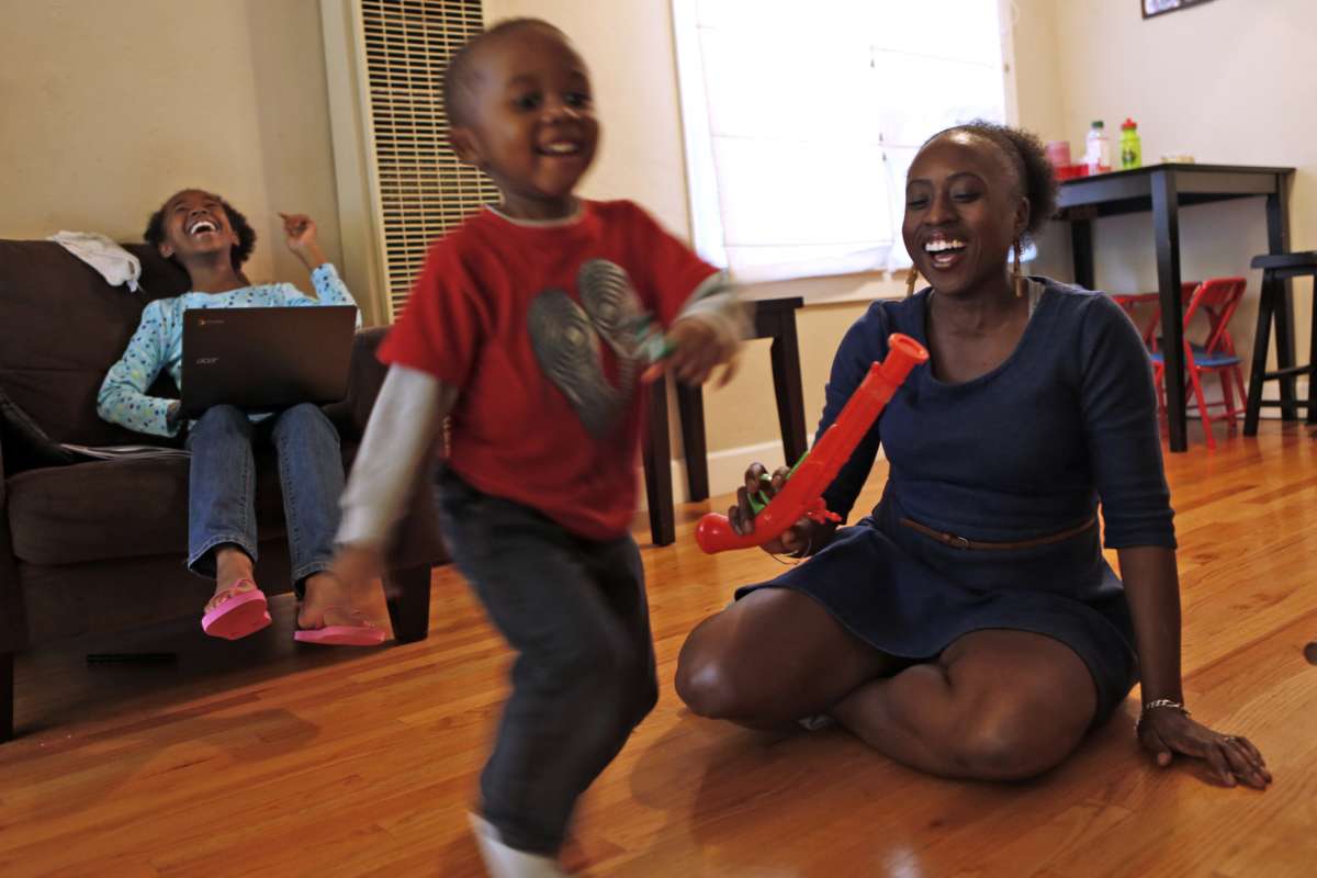 Family of three laugh together in living room.