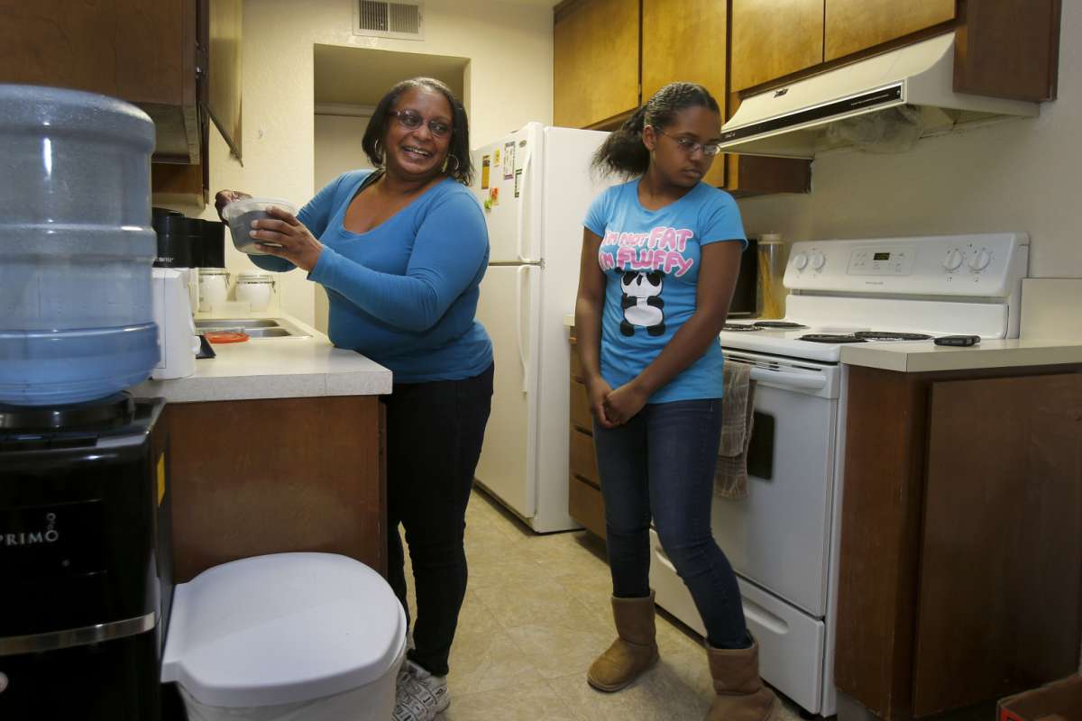 Mother and child prepare coffee in modest kitchen.
