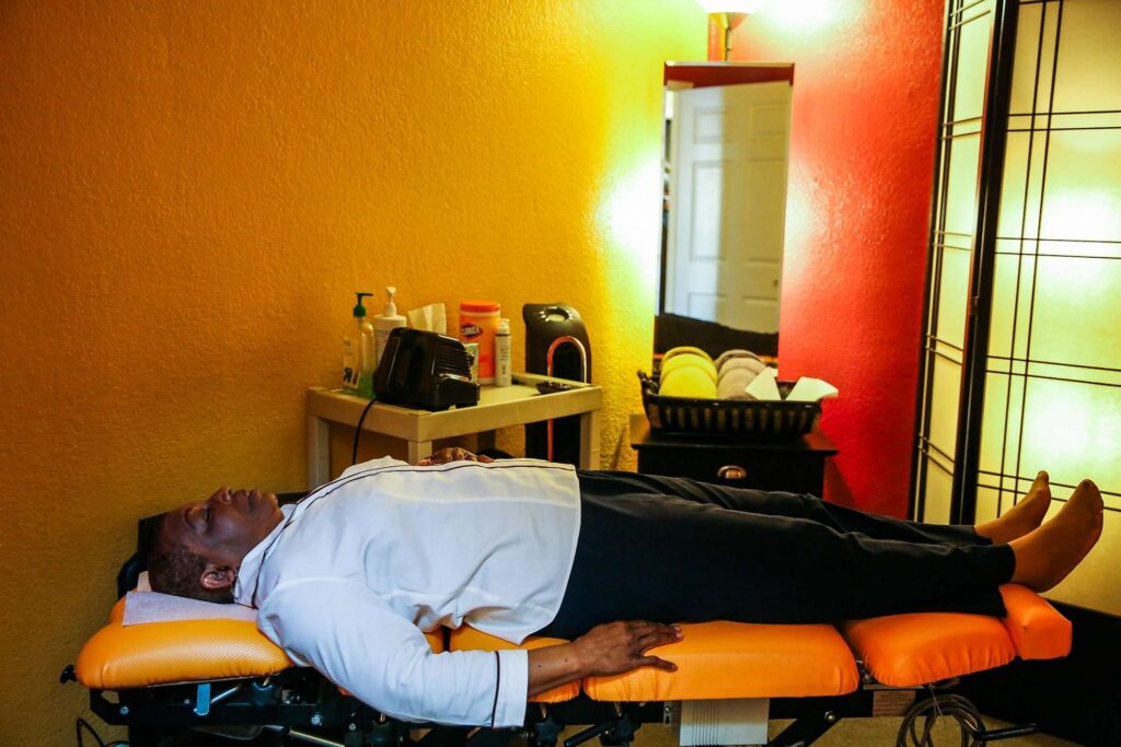 Woman lying on chiropractor table in warmly lit room, resting peacefully.