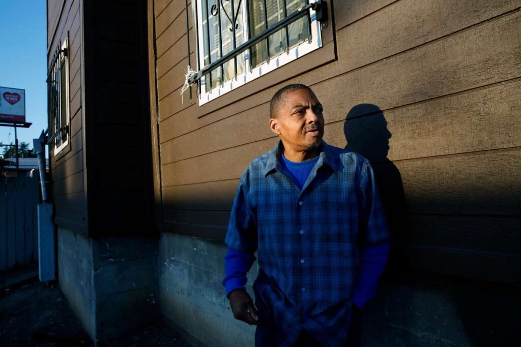 Man standing in front of an apartment building, gazing thoughtfully.
