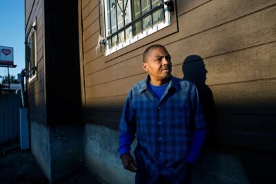 Man standing in front of an apartment building, gazing thoughtfully.