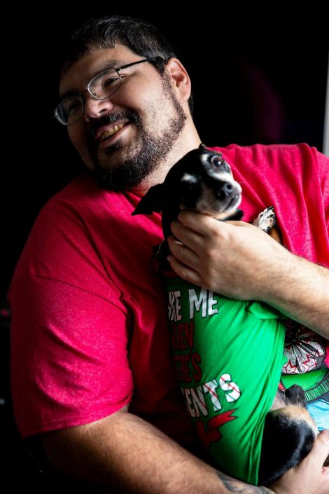 Man holds small dog in lap while smiling.