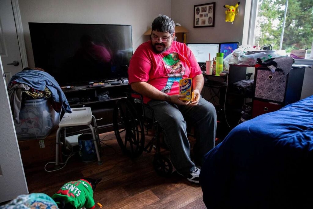 Man in wheelchair in bedroom with pet dog.