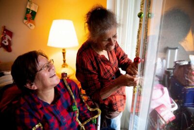 Two woman decorate for holidays indoors.