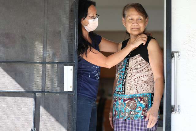 Woman helps an older woman put necklace on in doorway.
