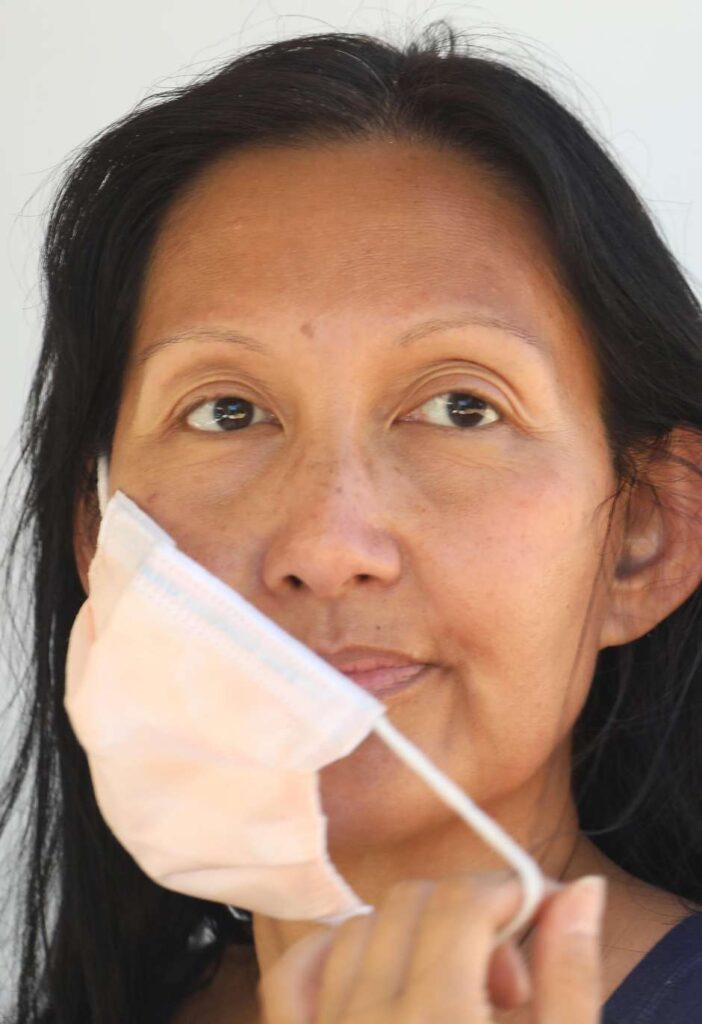Close-up of a woman adjusting a face mask and looking forward.