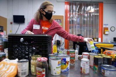 Woman wearing a mask distributes canned food at a food pantry.