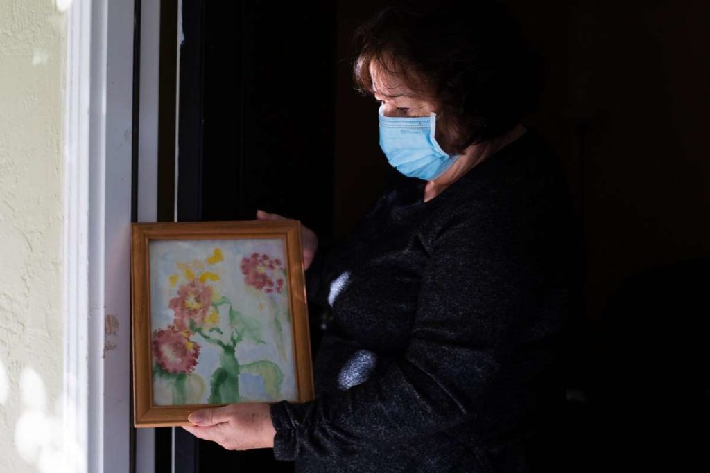 Woman wearing a mask holds up a drawing in a dim room.
