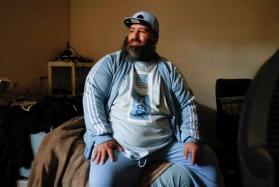 A man sits on a bed, smiling gently—highlighting personality and calmness.