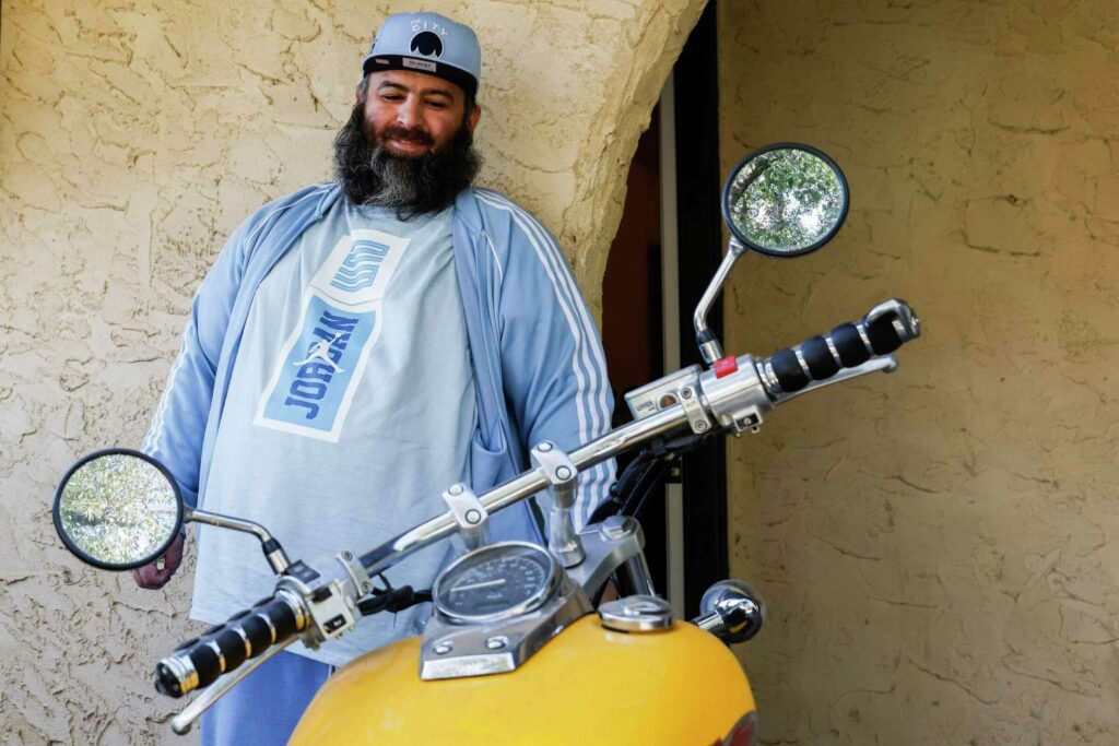 A man poses proudly with a motorcycle—expressing independence and passion.