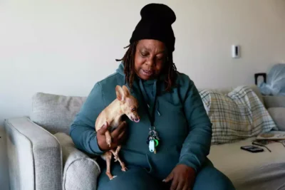 Woman sitting on a couch holding a small dog and smiling.