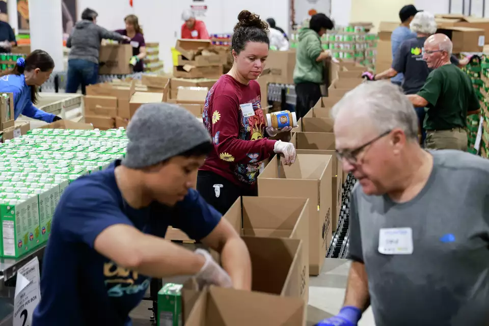 Volunteers pack supplies into boxes at food bank—demonstrating community support.
