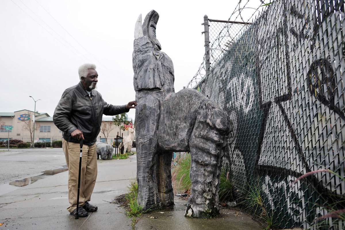 Man with walking cane touches wooden figure of elephant.