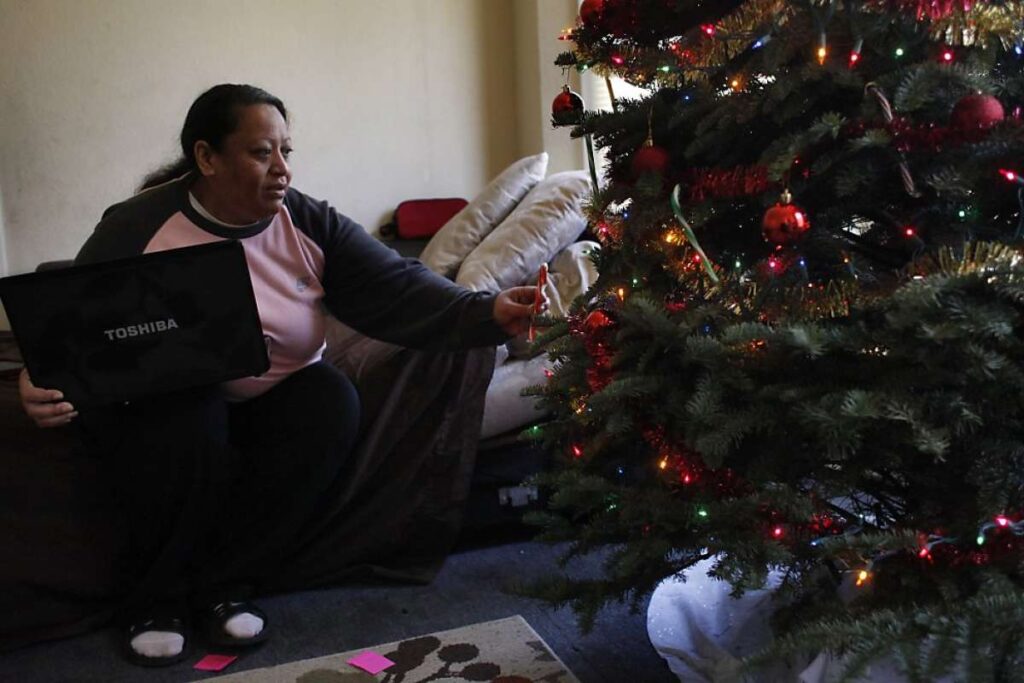 Woman holding laptop on couch next to Christmas tree.