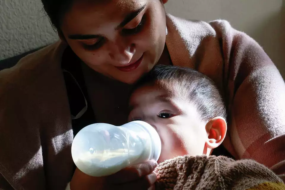 A mother holds a baby while feeding with a bottle—highlighting nurturing in daily life.