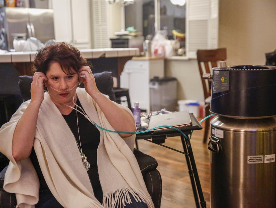 A woman sits next to oxygen tank, applying medical wear—conveying determination and resilience.