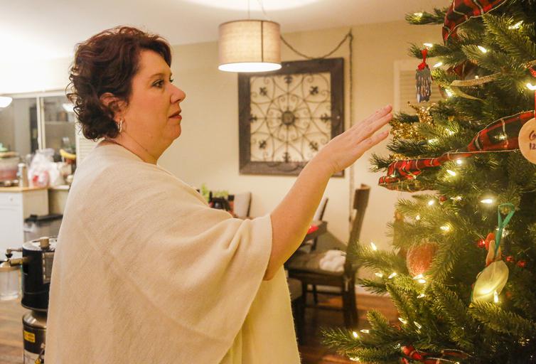 A woman decorates a Christmas tree, smiling—highlighting celebration and hope.