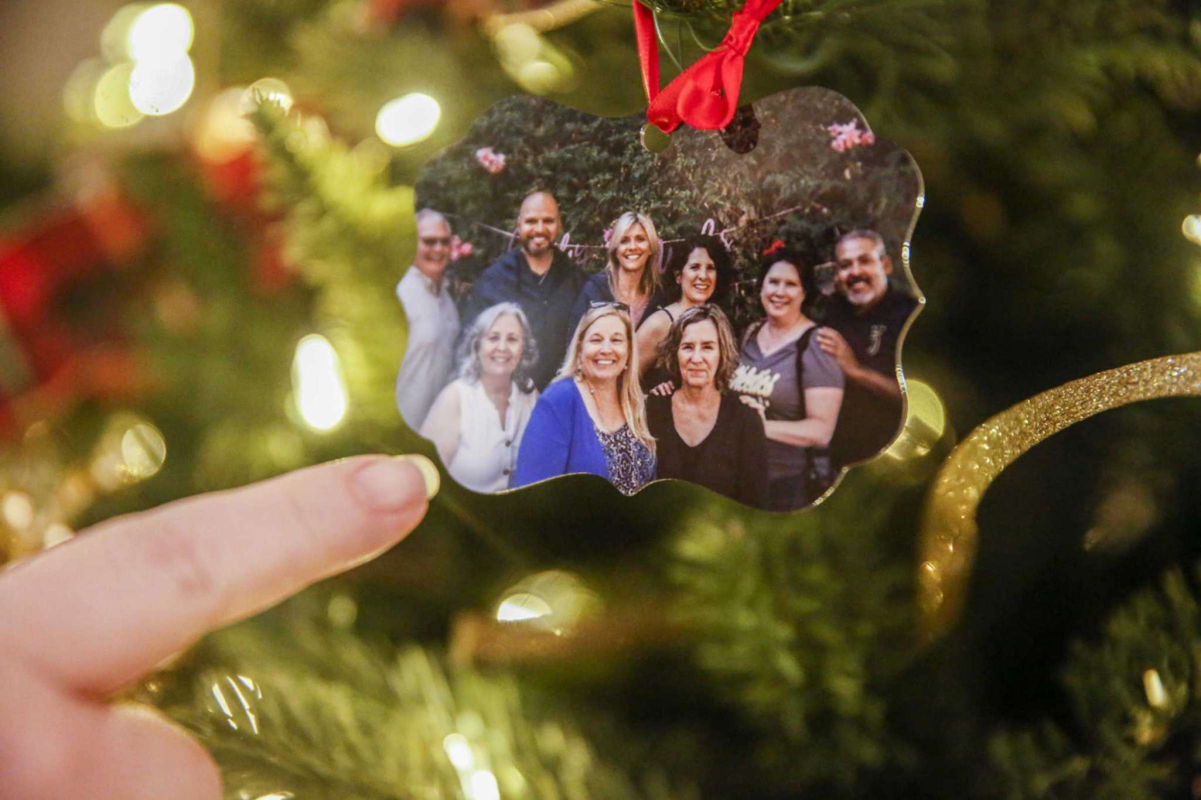 A close-up of a hand pointing at a holiday ornament with a family portrait—capturing tradition and memory.