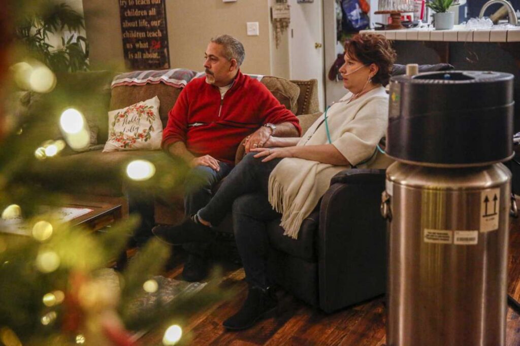 A man and woman sit on a couch during the holidays, holding hands—showcasing togetherness and joy.