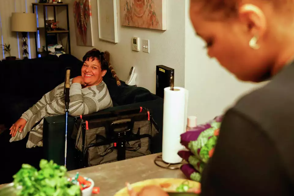 A woman sitting on a couch smiles at a table, chatting with someone—representing inclusion and warmth.
