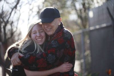 Elderly person and woman hugging outdoors.