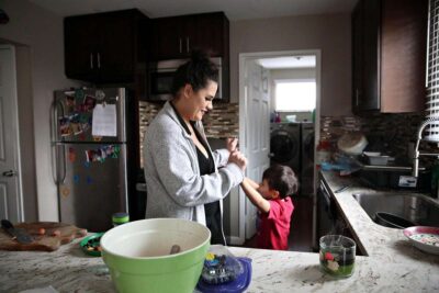 Woman cooking in a kitchen while a child stands nearby.