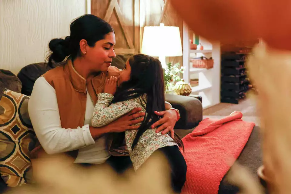 A woman and young girl share a hug on a couch—conveying affection, trust, and comfort.