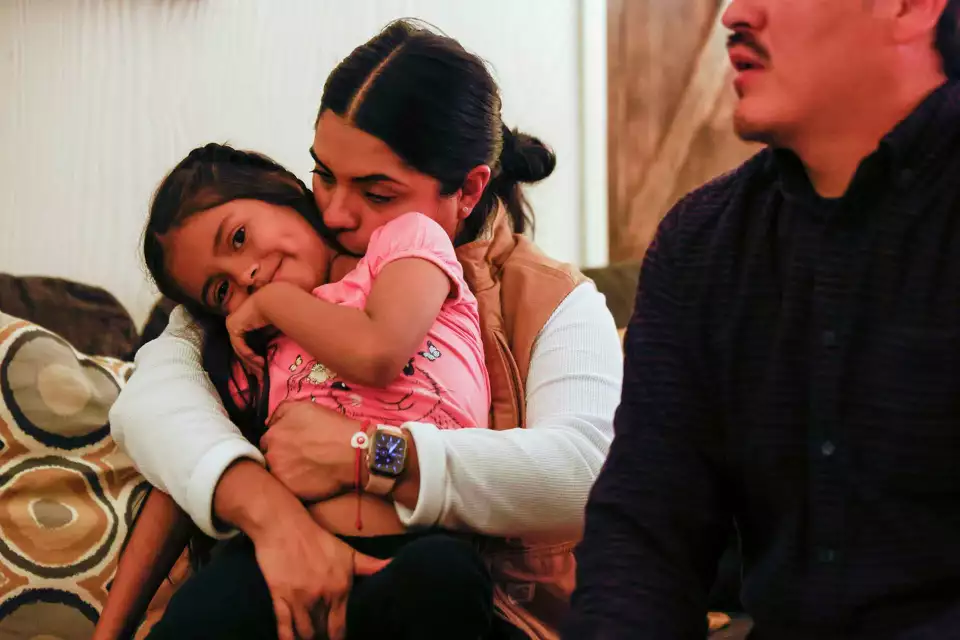 A woman hugs a child while sitting on couch—offering love and stability.