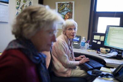 Two elderly women working in a community office setting.