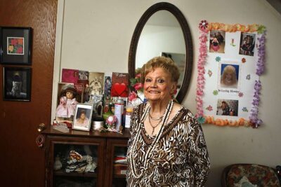 Elderly woman poses in front of mirror for a picture.