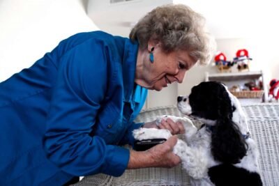 Elderly woman smiling at pet dog on couch.