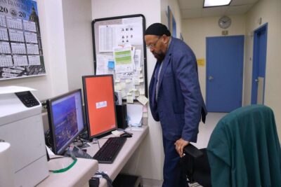 Man works at a desk with computer screens in a office setting.