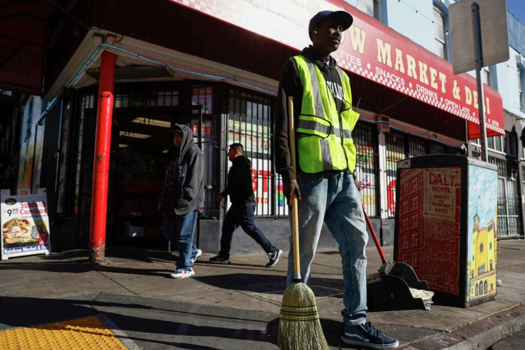 A man sweeps in front of a market—representing community upkeep.