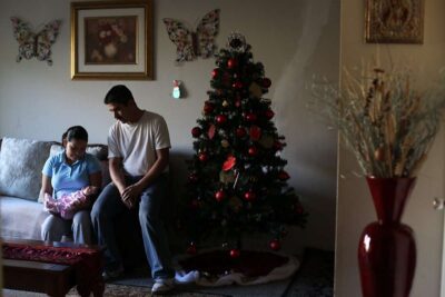 Couple holds newborn baby on couch next to Christmas tree.