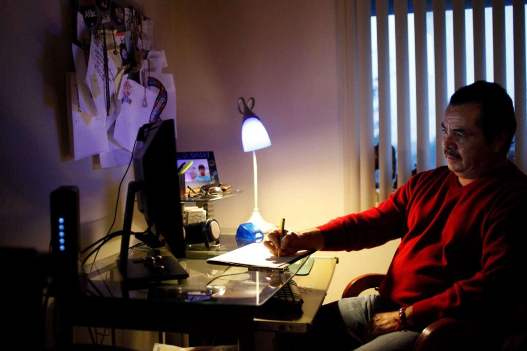 Man sits at computer desk writing in notepad.