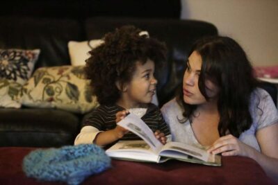 Mother and child read book together on couch.