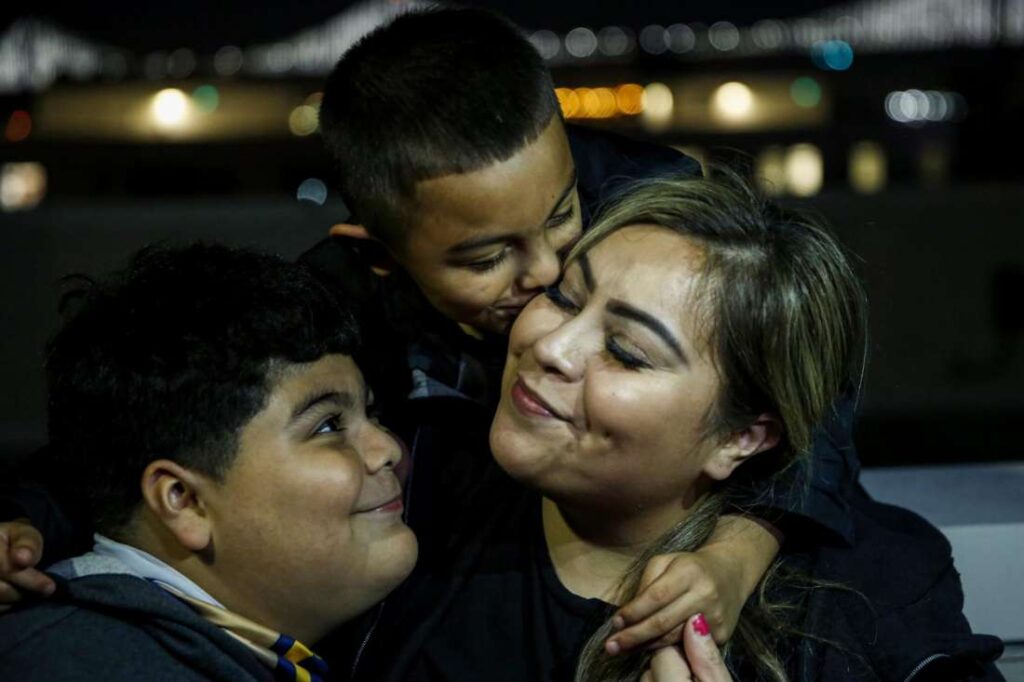 A woman smiles as two children affectionately hug her—highlighting love, closeness, and multigenerational bond.