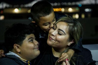 A woman smiles as two children affectionately hug her—highlighting love, closeness, and multigenerational bond.