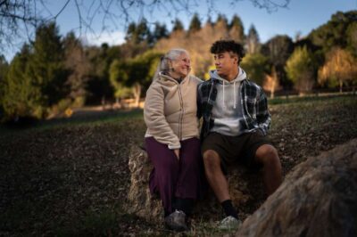 Mother and son sitting outdoors on a bench surrounded by trees.