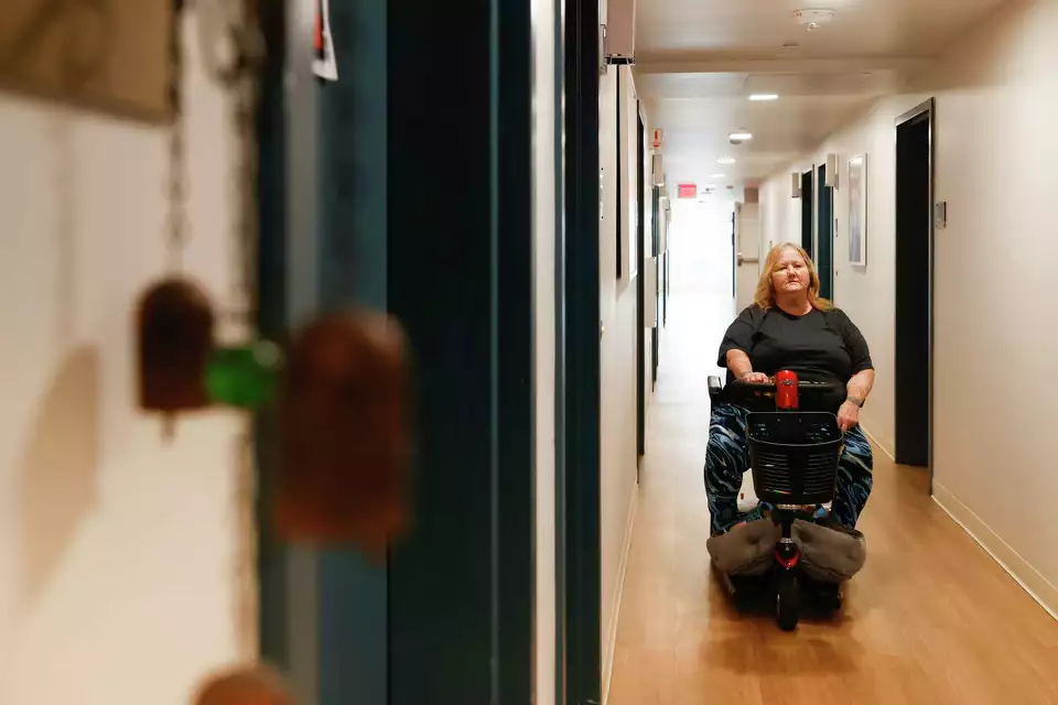 A woman in a power wheelchair moves down a hallway—emphasizing access, movement, and personal freedom.