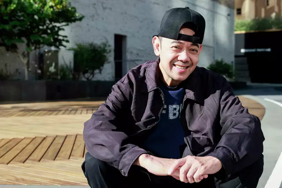 Man in a backward cap sitting outdoors, smiling.