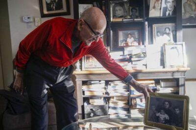 An older man carefully organizes books and photos on a shelf—symbolizing legacy and care.