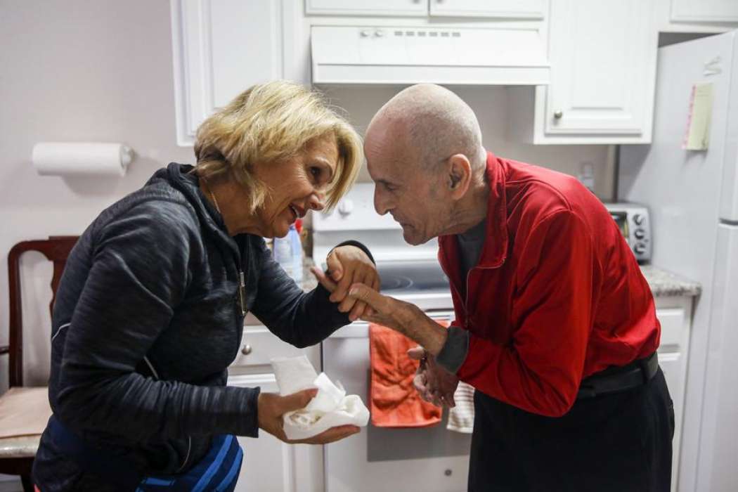 A woman and older man shake hands in modest kitchen—illustrating compassion and warmth.