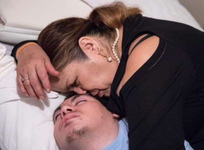 Woman comforting and gently resting her head on her son lying in bed.