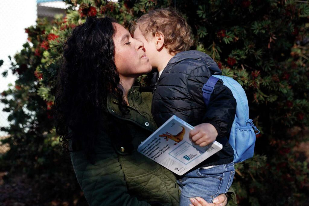 A woman kisses a child on the cheek while showing a book—representing love and learning.
